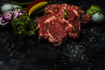 on a dark background fresh, red, raw beef and spilled coarse salt, next to it lies fresh vegetables