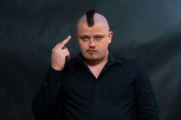 Punk with a mohawk in a black shirt. Finger pointing to his hairstyle. Facial expression is serious...