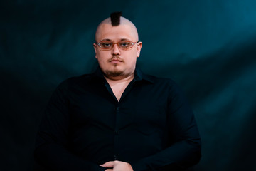 Punk with glasses looking at the lens. The face is serious and contented. Arms crossed on his stomach.