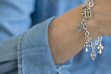 Close up photograph of a woman's silver bracelet of crosses against denim