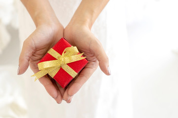 Close up hand of hands woman holding present a small red gift box wrapped with golden ribbon...
