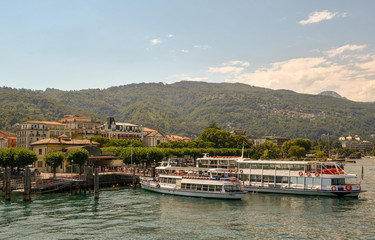 Fototapeta na wymiar Molo sul lago con traghetti, battelli e montagne sullo sfondo in estate, Stresa, Lago Maggiore, Piemonte, Italia