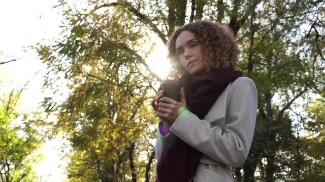 Autumn, a young woman in the park is drinking coffee or tea.