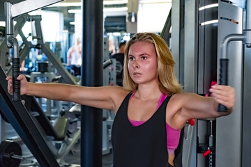 Fototapeta na wymiar Young fit woman at the gym doing exercise with horizontal chest press. Female athlete at a fitness room working out with seated chest press machine