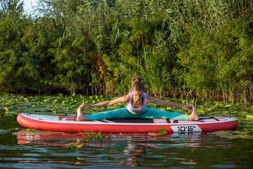Young woman are doing yoga on a stand up paddle board SUP on a beautiful lake or river