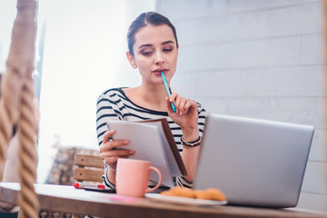 Thoughtful look. Nice smart woman looking at her notes while sitting in front of the laptop