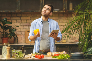 Man preparing delicious and healthy food in the home kitchen on a sunny day. Using tablet computer for searching recipes.