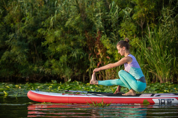 Fototapeta na wymiar Young woman are doing yoga on a stand up paddle board SUP on a beautiful lake or river