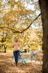 Young woman with bicycle using smartphone in autumn park