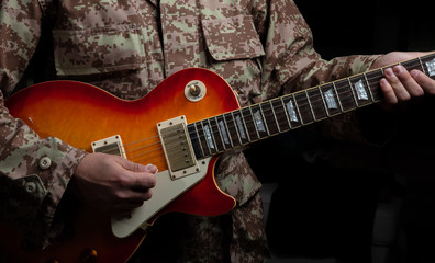 Young man in military uniform playing guitar, close up view, dark background