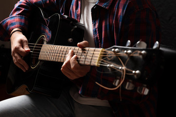 Obraz na płótnie Canvas Young man playing guitar, close up view, dark background