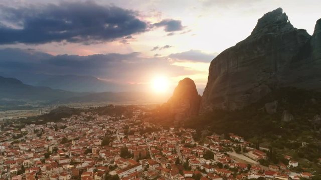 Panning aerial shot European small old city or suburb Kalampaka flying over fantastic landscape rock formation Meteora in central Greece at colored sunset and yellow big sun