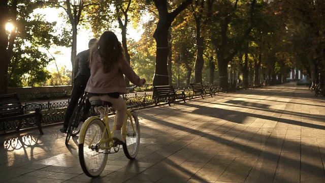 Rare view of a young happy couple or friends riding their bikes in the empty city park or boulevard in summertime. People, leisure and lifestyle concept