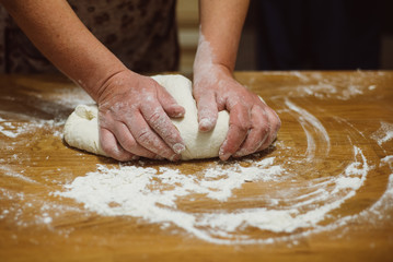 Hands kneading raw dough on wooden table