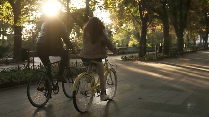 Rare view of caucasian young couple or friends riding their bikes in the empty city park or boulevard in summertime. People, leisure and lifestyle concept. Green trees around - Powered by Adobe