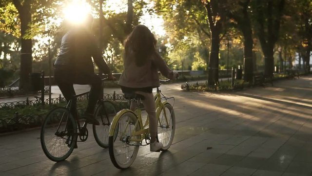 Rare view of caucasian young couple or friends riding their bikes in the empty city park or boulevard in summertime. People, leisure and lifestyle concept. Green trees around