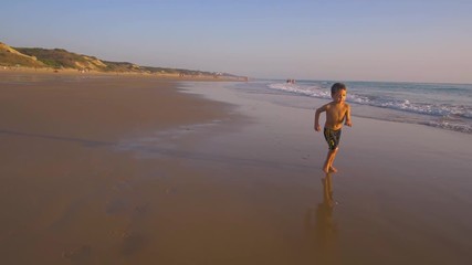 Slow motion - A child 3-5 years old running freely while the camera chase him and he laughs, in a sunny day in the beach 