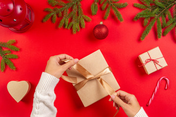 Christmas gift wrapping. Woman's hands packing Christmas present box on red table background