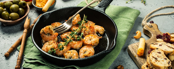 Prawns Shrimps roasted on frying cast iron pan with thyme and garlic. Party food background. Banner.