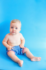 Beautiful baby in jeans panties sitting on blue background. Copy space. Baby emotions.