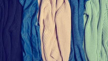 Stack of knitted sweaters and jeans close-up. Background of clothes. Women's wardrobe.