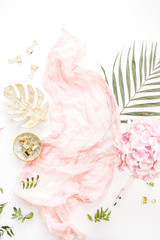 Stylish composition with pink hydrangea flowers bouquet, tropical palm leaf, pastel blanket, monstera leaf plate and accessories on white background. Flat lay, top view rose gold desk.