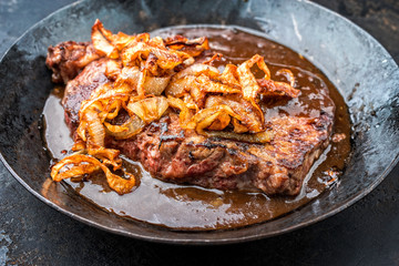 Traditional dry aged sliced roast beef with fried onion rings as closeup in a wrough-iron pan with brown sauce