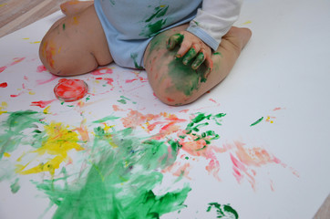 Painted colorful child hand against white background. girl draws her fingers multicolored paints on white paper. paint cans near