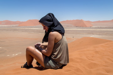 Jeune femme voyageuse assise sur une dune dans le désert de Sossusvlei en Namibie