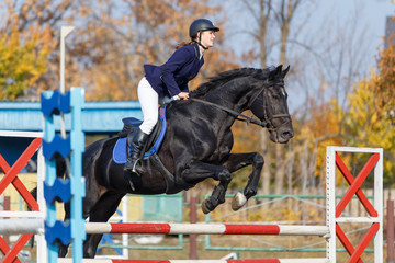 Young rider girl on horse jumping over obstacle