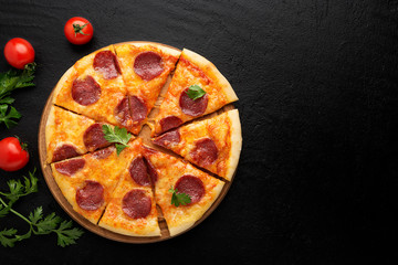 Pepperoni pizza, tomatoes and parsley. Tasty pepperoni pizza on black stone background. Overhead view of italian pizza.