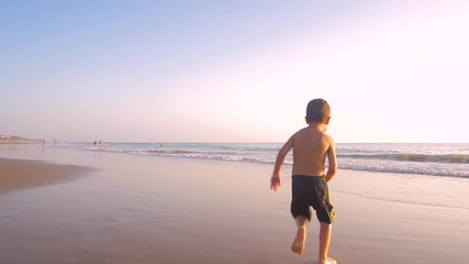 Slow motion - A child 3-5 years old running freely while the camera chase him and he laughs, in a sunny day in the beach 