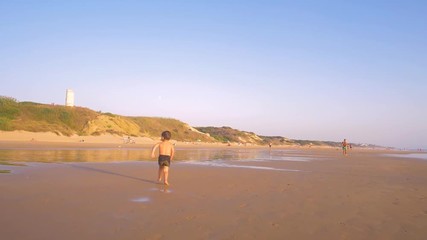 Slow motion - A child 3-5 years old running freely while the camera chase him and he laughs, in a sunny day in the beach 
