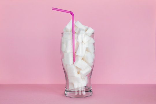 Glass full of sugar cubes over pink background. Unhealthy diet and diabetes concept.