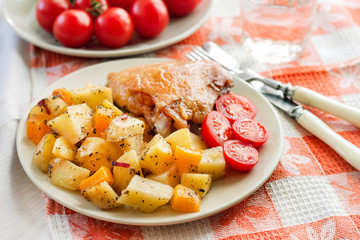 Baked chicken thigh with baked potatoes and pumpkin garnish on a plate