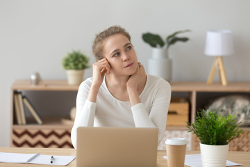Thoughtful millennial young female sitting at the desk in office room or home opposite computer....