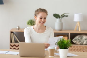 Young millennial satisfied woman sitting at the desk in office room, at home. Glad worker female...