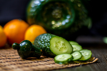 on the table is a vase, cucumbers and tangerines.