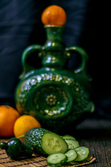 on the table is a vase, cucumbers and tangerines.