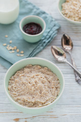 Oatmeal porridge bowl on the white wooden background.