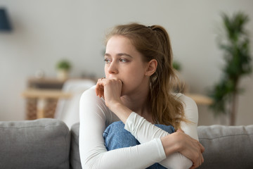 Head shot woman anxious worried woman sitting on couch at home. Frustrated confused female feels...