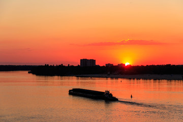 Tugboat pushing a heavy long barge on the river Dnieper at sunset