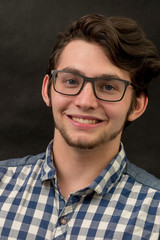 Obraz premium Portrait of Handsome European Young man in spectacles, isolated over black background. The smiling young male wears glasses and a blue shirt.