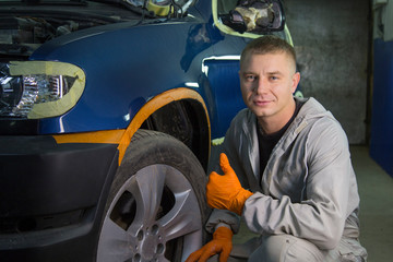 Repair and painting car car mechanic. Auto mechanic worker painting car in a paint chamber during repair work. Auto repairman plastering autobody bonnet. 