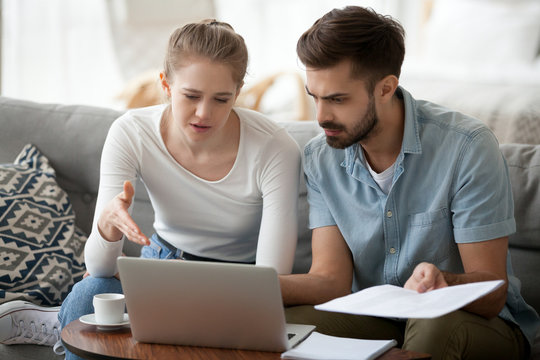 Frustrated married couple has financial problems wife and husband received bad news from bank about debt high taxes. Millennial woman and man reading mail on laptop holding paper letter domestic bill