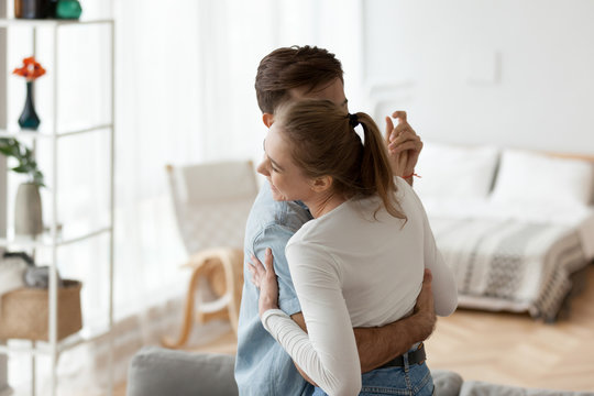 Millennial couple in love spend free time together at home. Man gently embracing beloved woman dancing waltz close each to other. Having romantic mood, relationships. Concept of date living together
