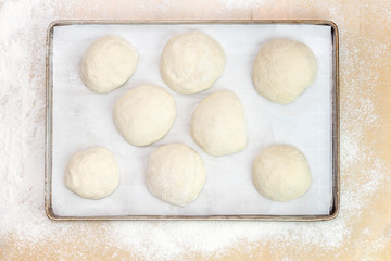 Balls of dough on parchment paper, on a metal tray on a wooden table covered with white flour