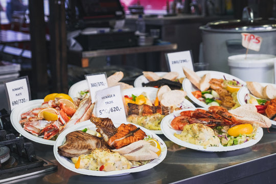 Delicious plates with a variety of grilled fish and seafood with mashed potatoes served with salad and a lemon wedges. Street Food ready to eat with price tag at Bergen Fish Market, Norway