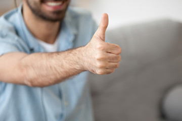 Close up happy cheerful friendly caucasian male showing giving thumbs up sign smiling at camera, focus on human hand, finger up. Hand gesture symbol of success and approval, meaning of like concept