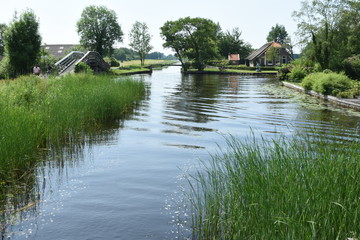 Fototapeta na wymiar beschoeid kanaal met fietspaden en boerderijen met rieten daken aan weerszijden in de buurt van Giethoorn